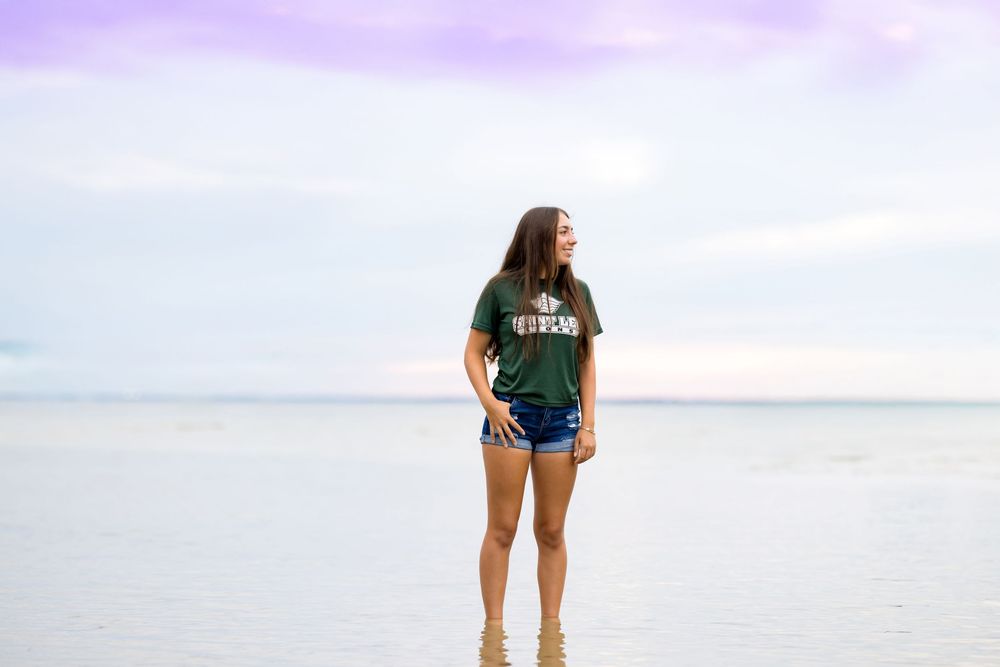 Standing in shallow water at sunset wearing casual summer attire.
