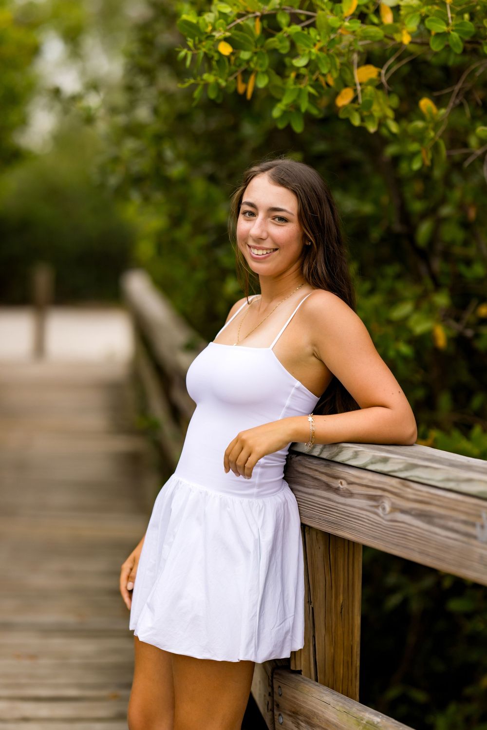 Summer portrait on boardwalk with white dress and natural greenery background.