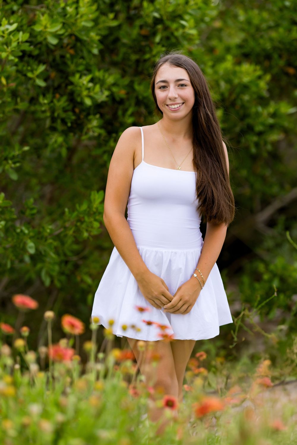 Woman in white summer top posing near orange wildflowers and green foliage.