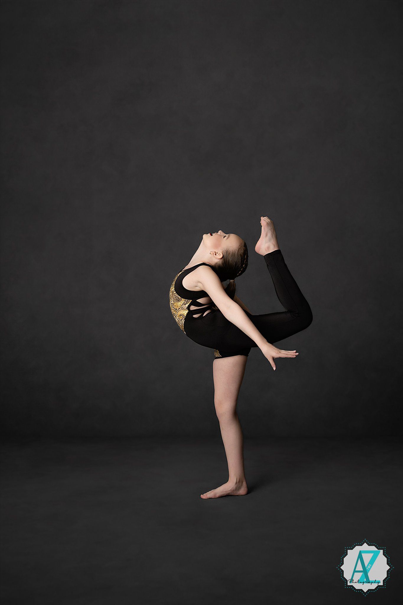 Dancer performs a standing backbend pose in a black leotard against dark background in artistic studio photography.