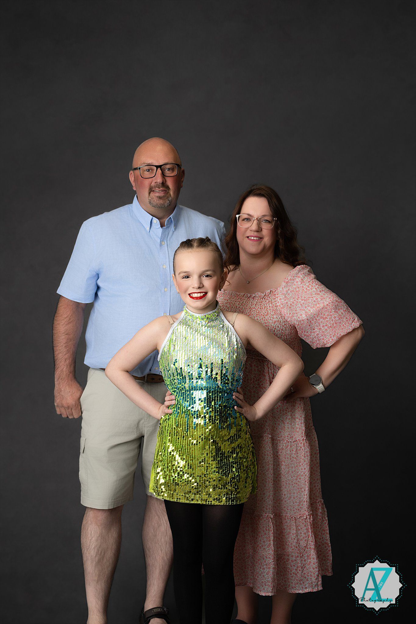 Three people pose against a dark background in casual attire with one wearing a sparkly green sequined dress.