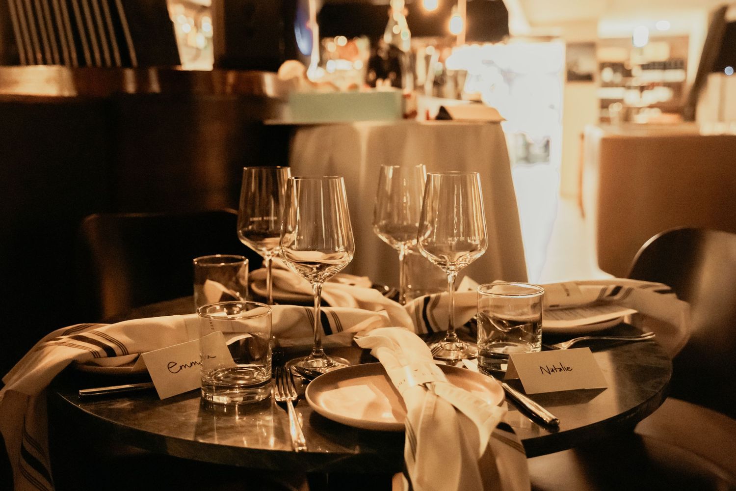 Elegant table setting in warm lighting with wine glasses and napkins arranged in an upscale restaurant atmosphere.