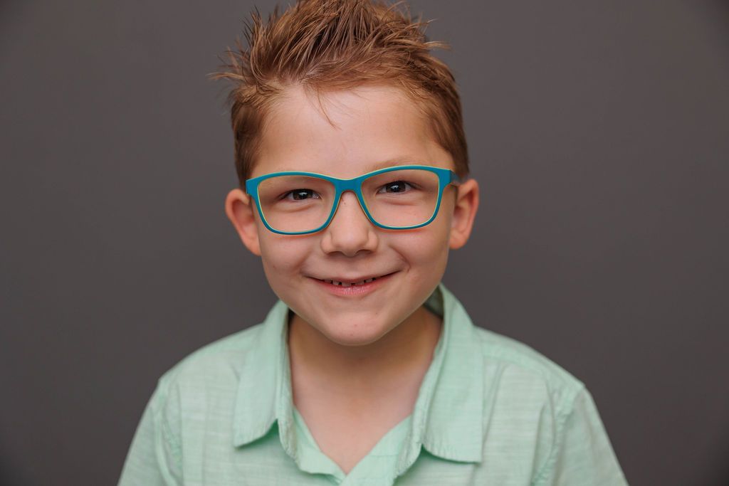 Professional headshots showing a bright smile and turquoise glasses against a gray studio backdrop.