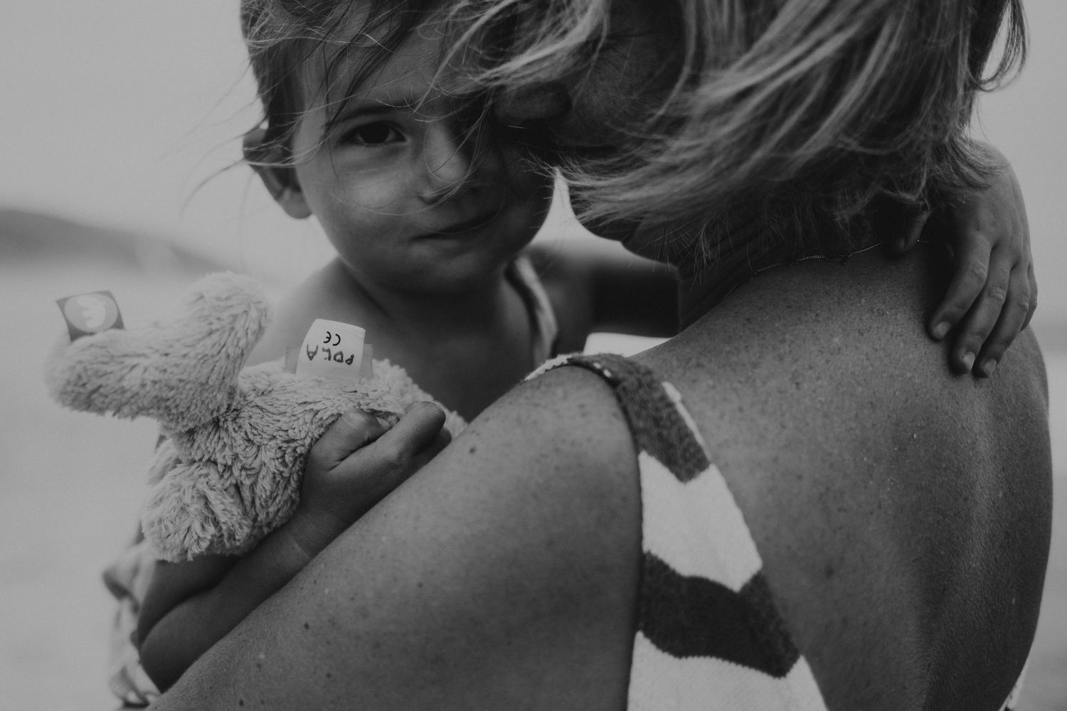 Mãe e filha em momento de  amor  na praia em uma foto preto e branco com luz difusa em uma sessão fotográfica de família em Peniche Portugal