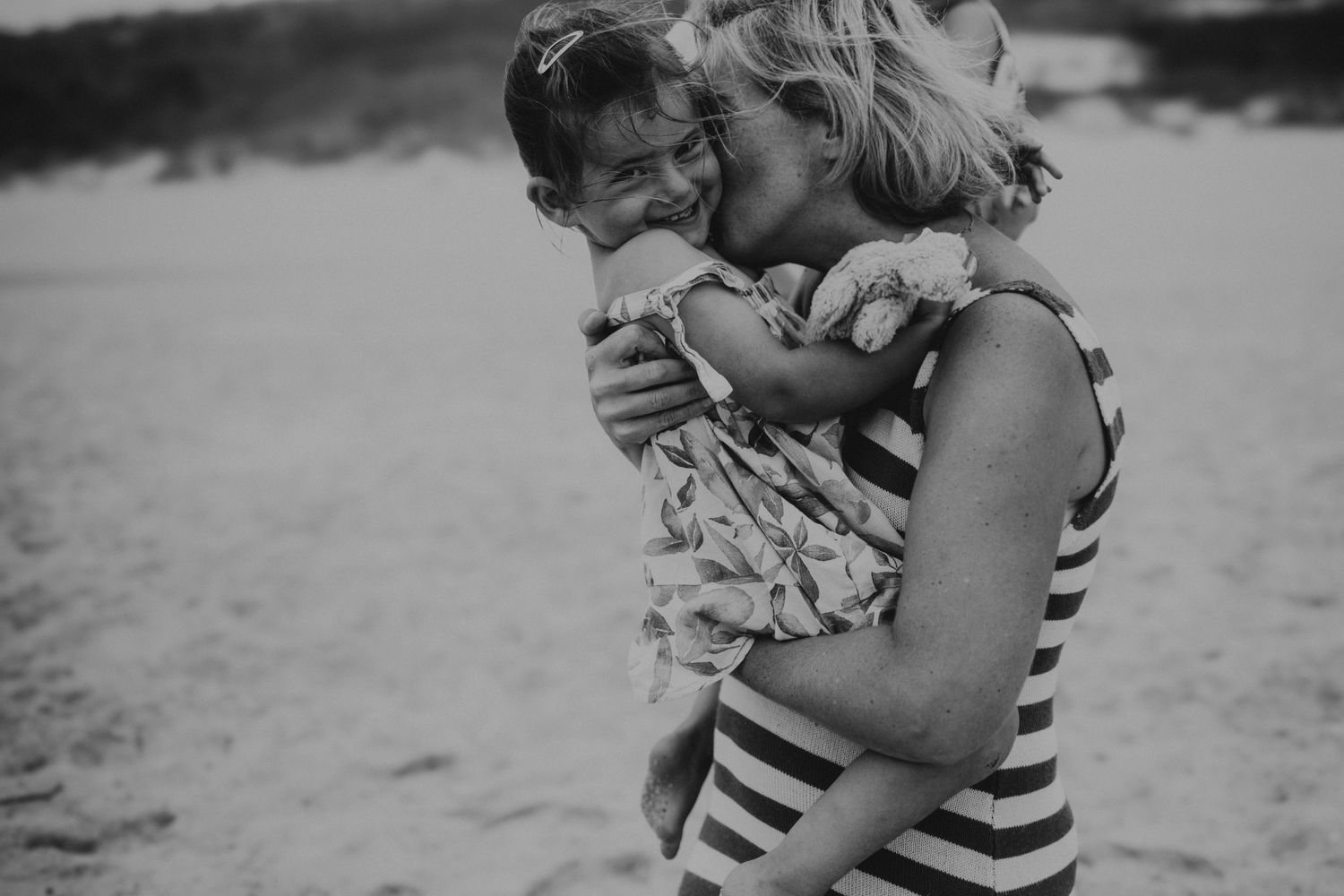 Mãe e filha em momento de  amor  na praia em uma foto preto e branco com luz difusa em uma sessão fotográfica de família em Peniche Portugal