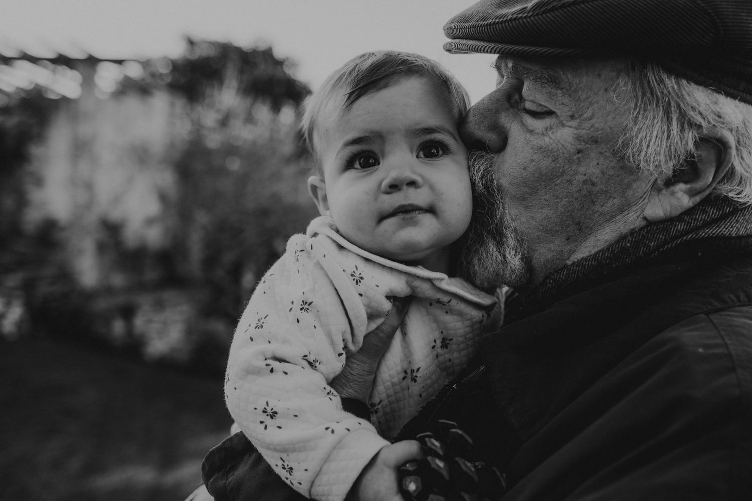 Bebé ganha um beijo do avô em uma foto em preto e branco no jardim da casa numa sessão de familia em Portugal , Óbidos