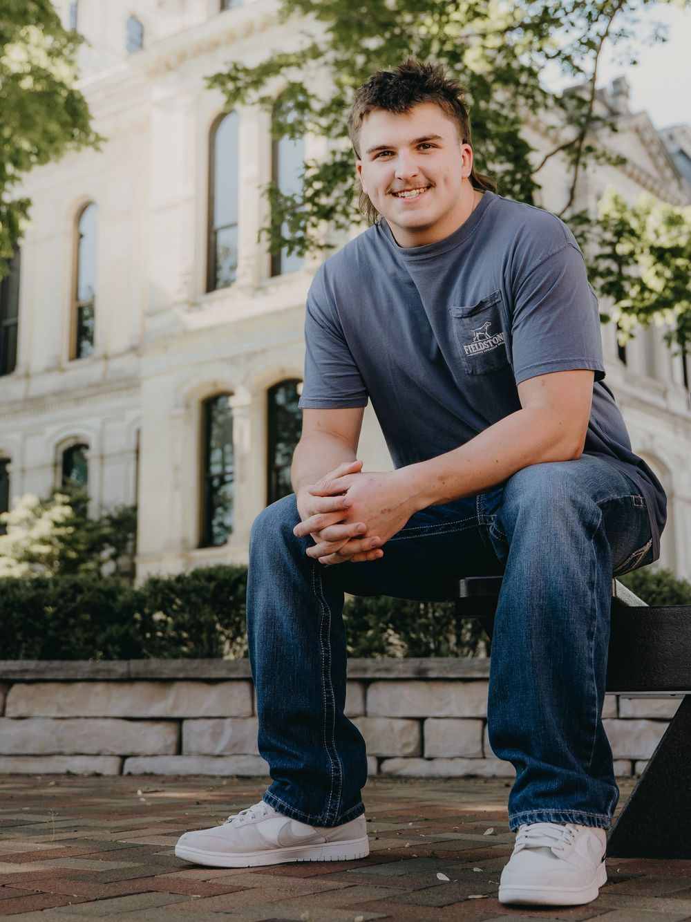 Casual outdoor Senior Portrait on stone bench with architectural building in background - Warsaw, Indiana