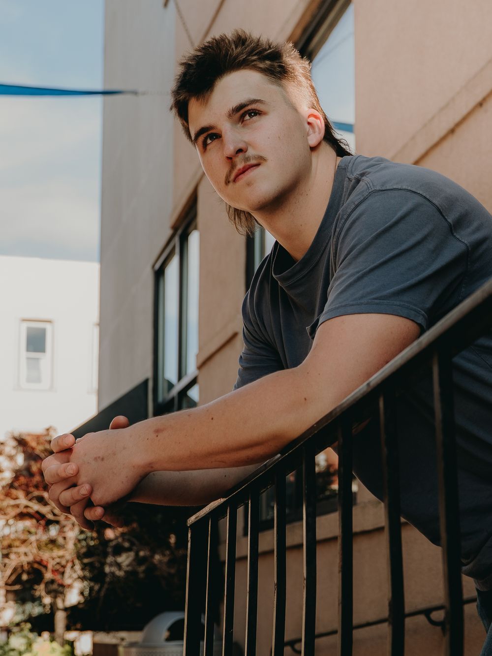Senior Portrait leaning on metal railing in grey t-shirt during golden hour - Warsaw, Indiana