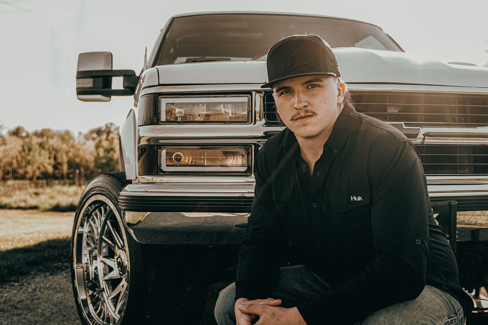 Senior Portrait showing chrome headlights and wheels with someone in black attire posing beside a truck in warm lighting - Warsaw, Indiana