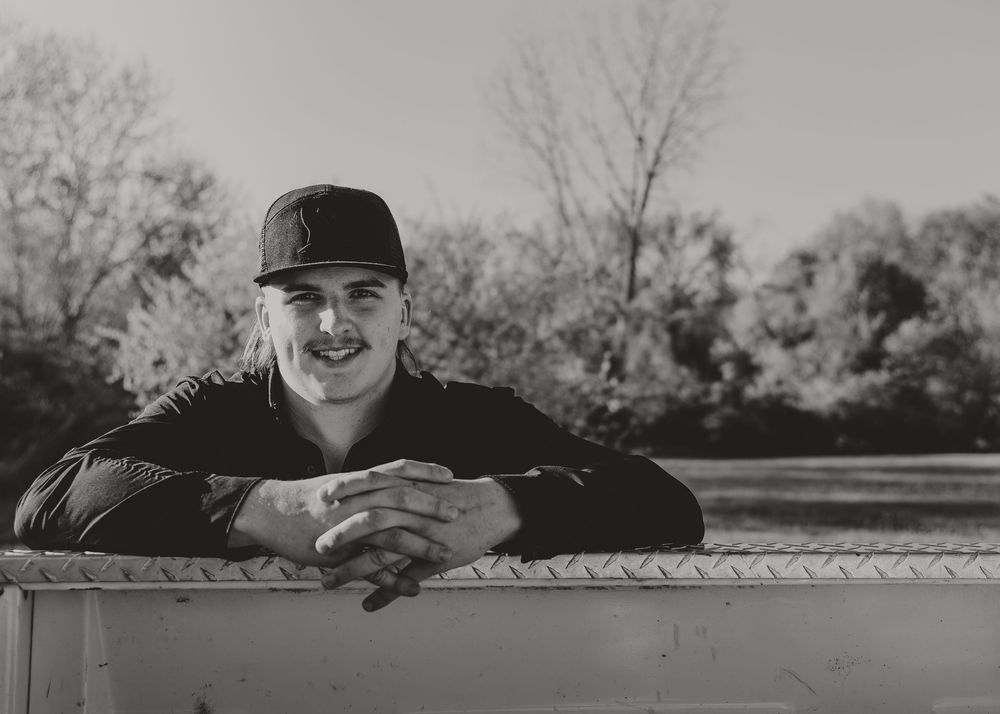 Black and white Senior Portrait showing them leaning on a truck bed railing in casual attire - Warsaw, Indiana