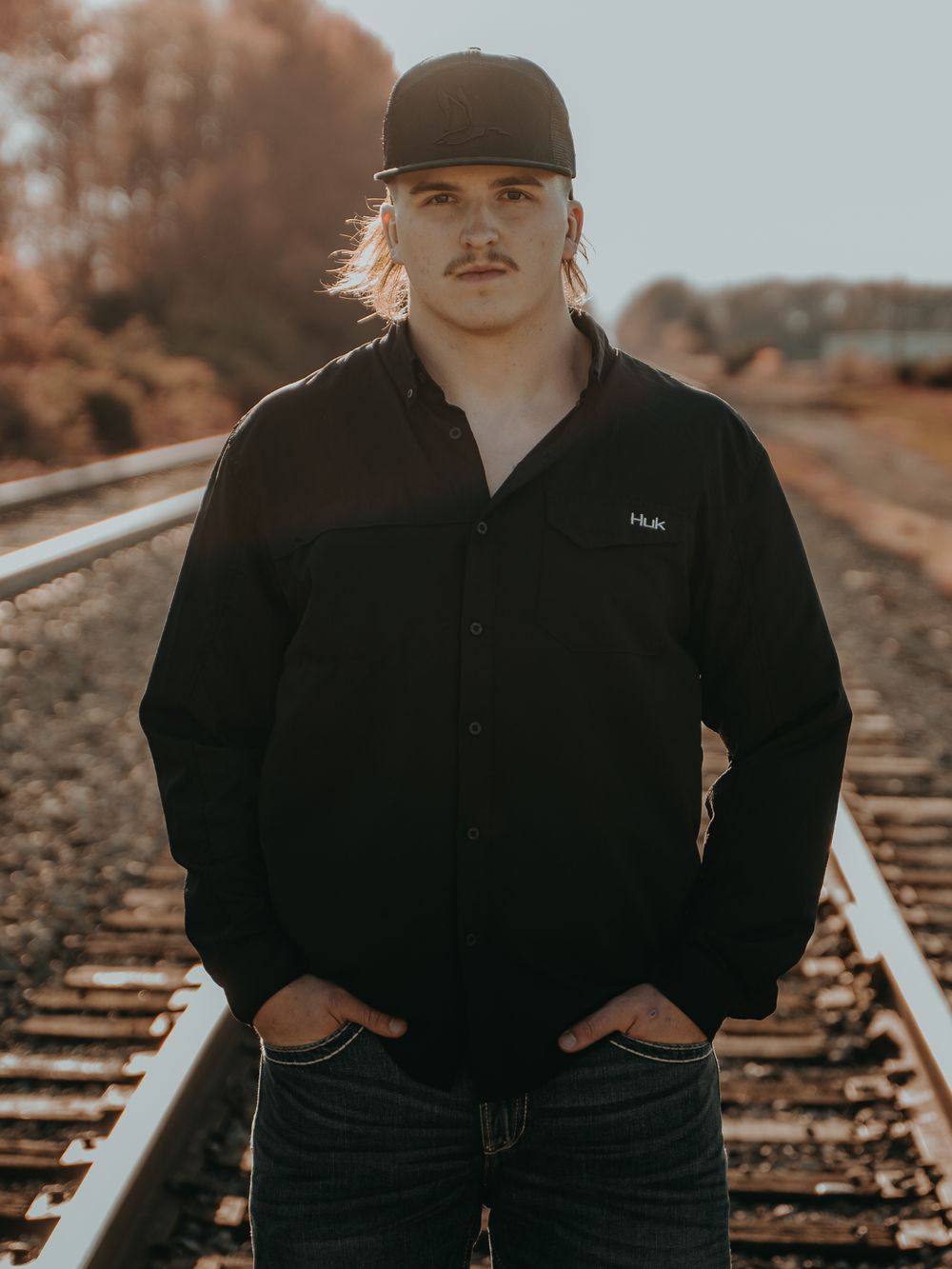 Senior Portrait at the railroad tracks with autumn colors showing senior in dark jacket and baseball cap - Warsaw, Indiana