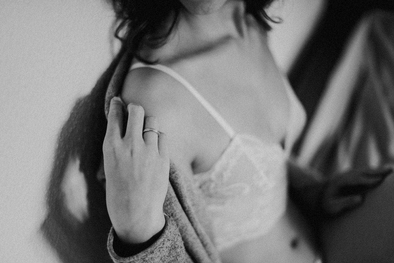 Person in Unterwäsche und Strickjacke lehnt an einer Wand. Schwarz-weiß-Fotografie mit Fokus auf die Schulter und Hand.