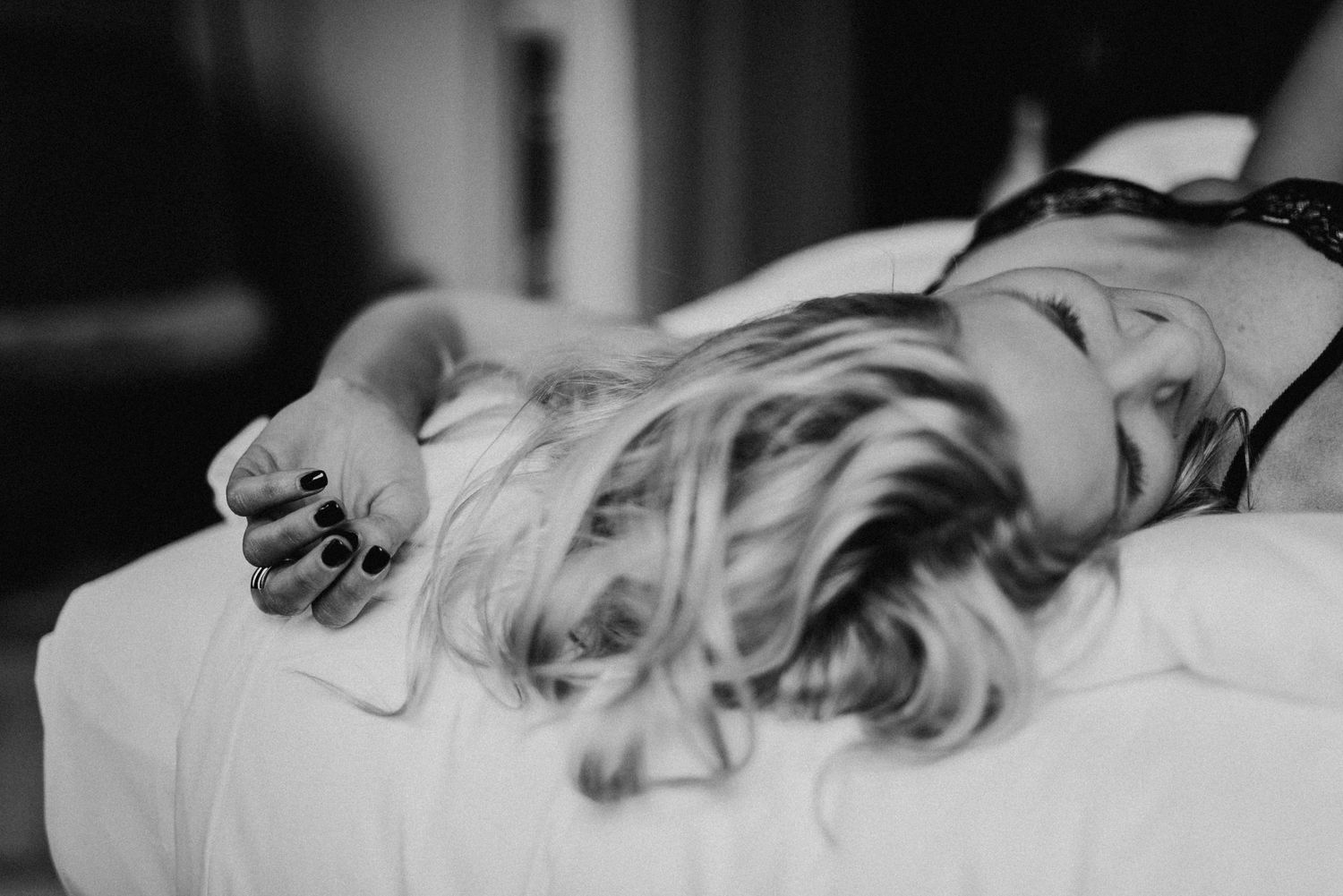 Frau mit blonden Haaren liegt entspannt auf einem Bett. Schwarz-weiß-Foto mit Fokus auf ihre Hand und Haare.