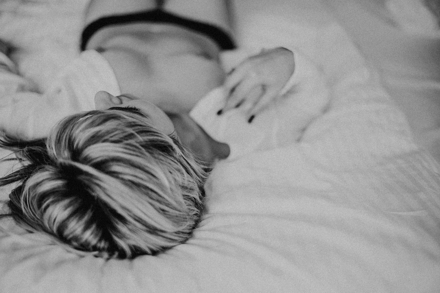 Person mit gestreiftem Haar liegt entspannt auf einem Bett, trägt ein weißes Hemd und schwarze Unterwäsche. Schwarz-Weiß-Foto.