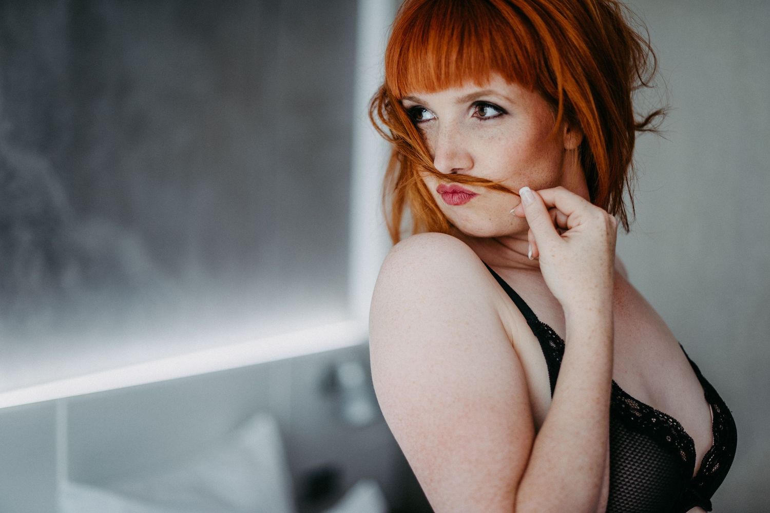 Rothaarige Frau in schwarzer Unterwäsche posiert verspielt für eine Boudoir Aufnahme.