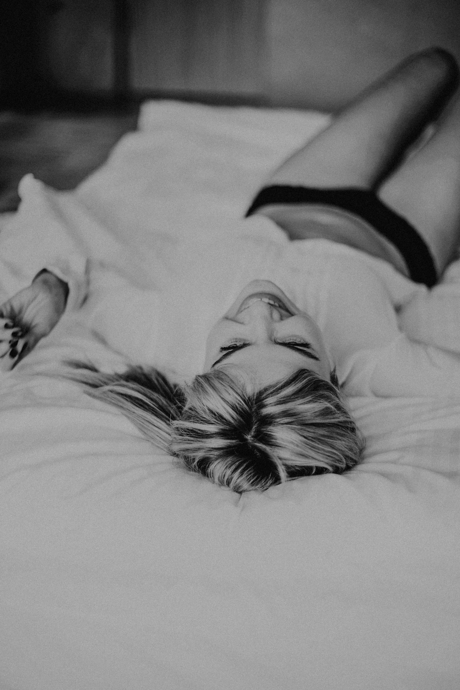Frau liegt entspannt auf einem Bett, trägt ein weißes Oberteil und dunkle Shorts. Schwarz-weiß Fotografie mit Fokus auf Ruhe.