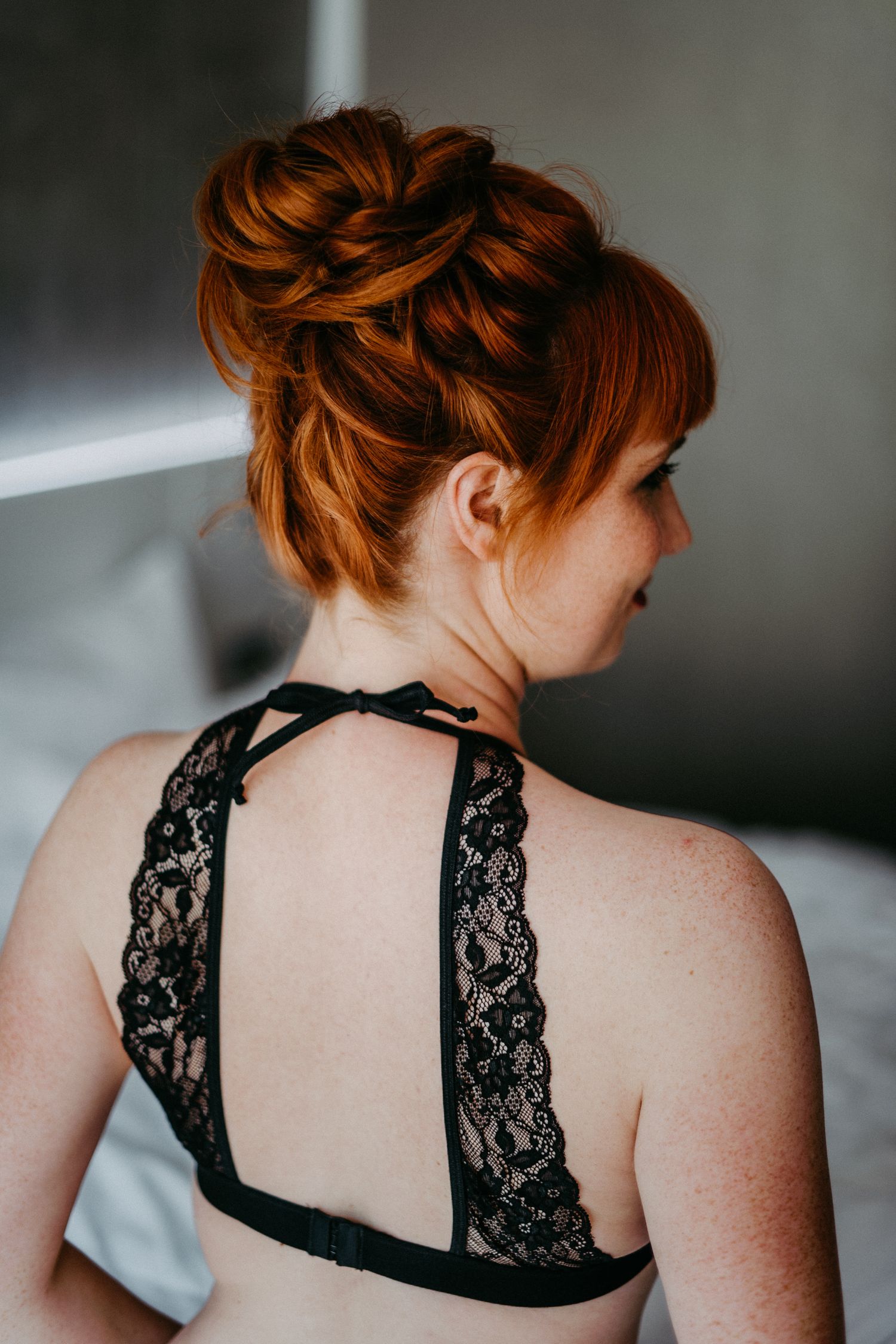 Eine Frau mit feurig roten Haaren posiert auf einem Bett. Sie trägt schwarze Unterwäsche und ist von hinten abgebildet. Boudoir foto Münster