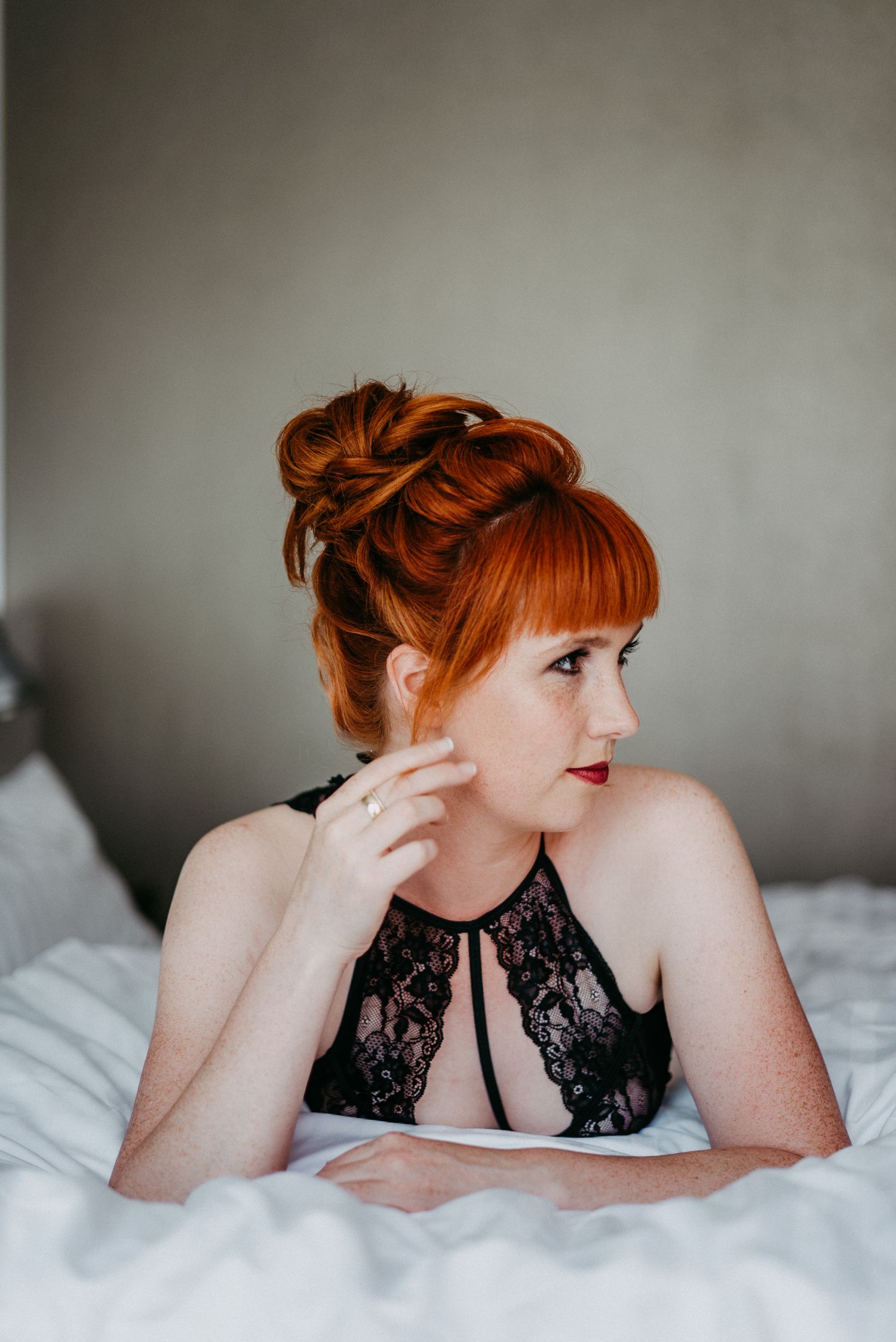 Frau mit leuchtend roten Haaren liegt auf einem Bett. Sie trägt schwarze Unterwäsche und schaut zur Seite. Boudoir Fotoshooting.