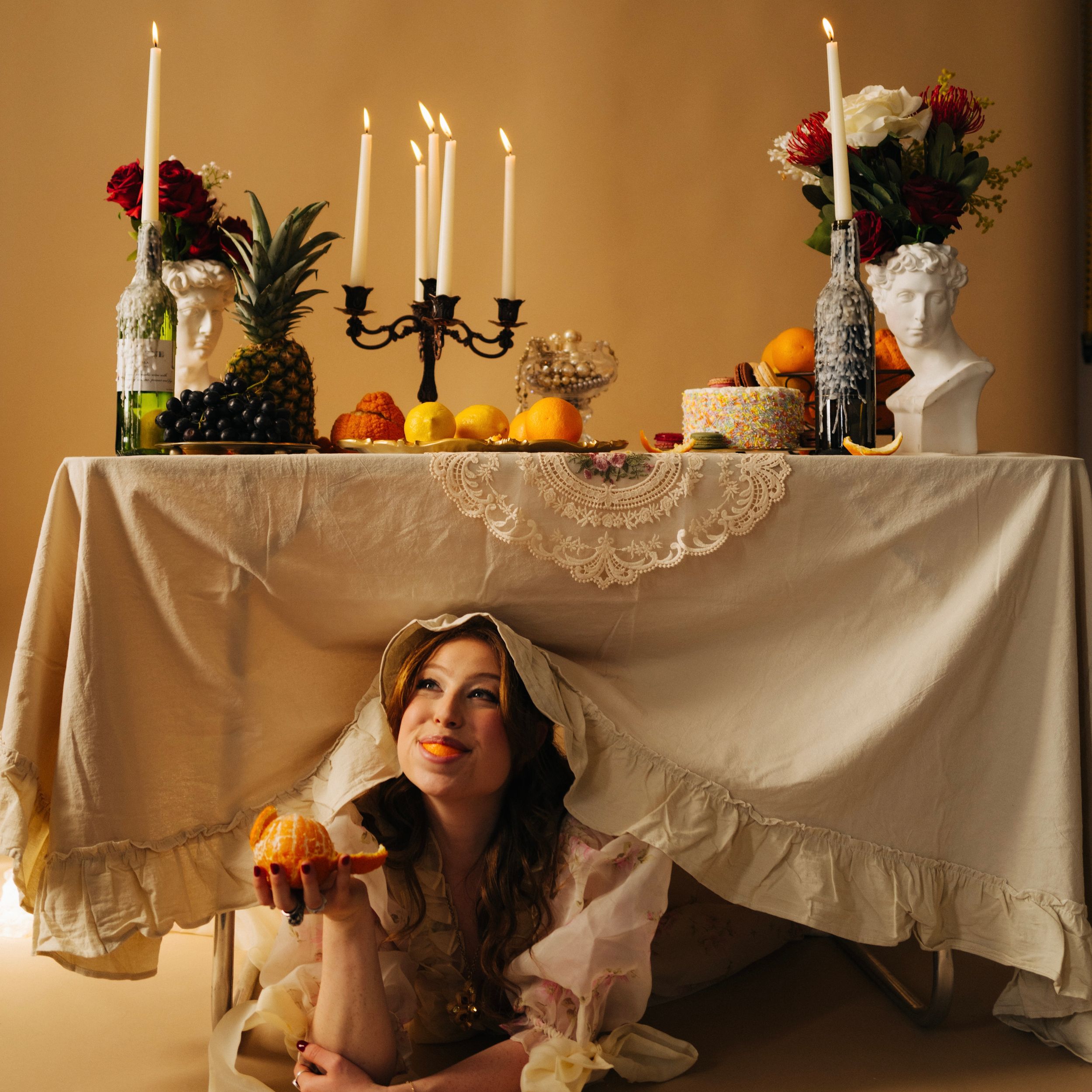 Still life setup with candle holder, fruits and floral arrangements on table with elegant white tablecloth.