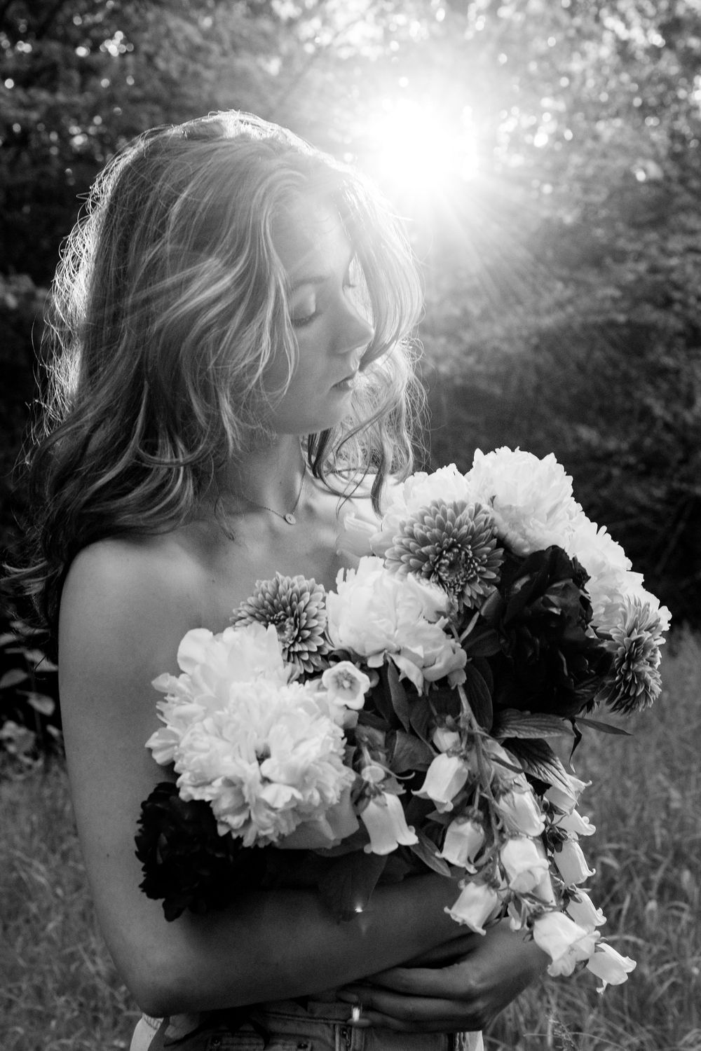 Elegant black and white photo of flowing hair and white peonies illuminated by dramatic sunlight in nature setting.