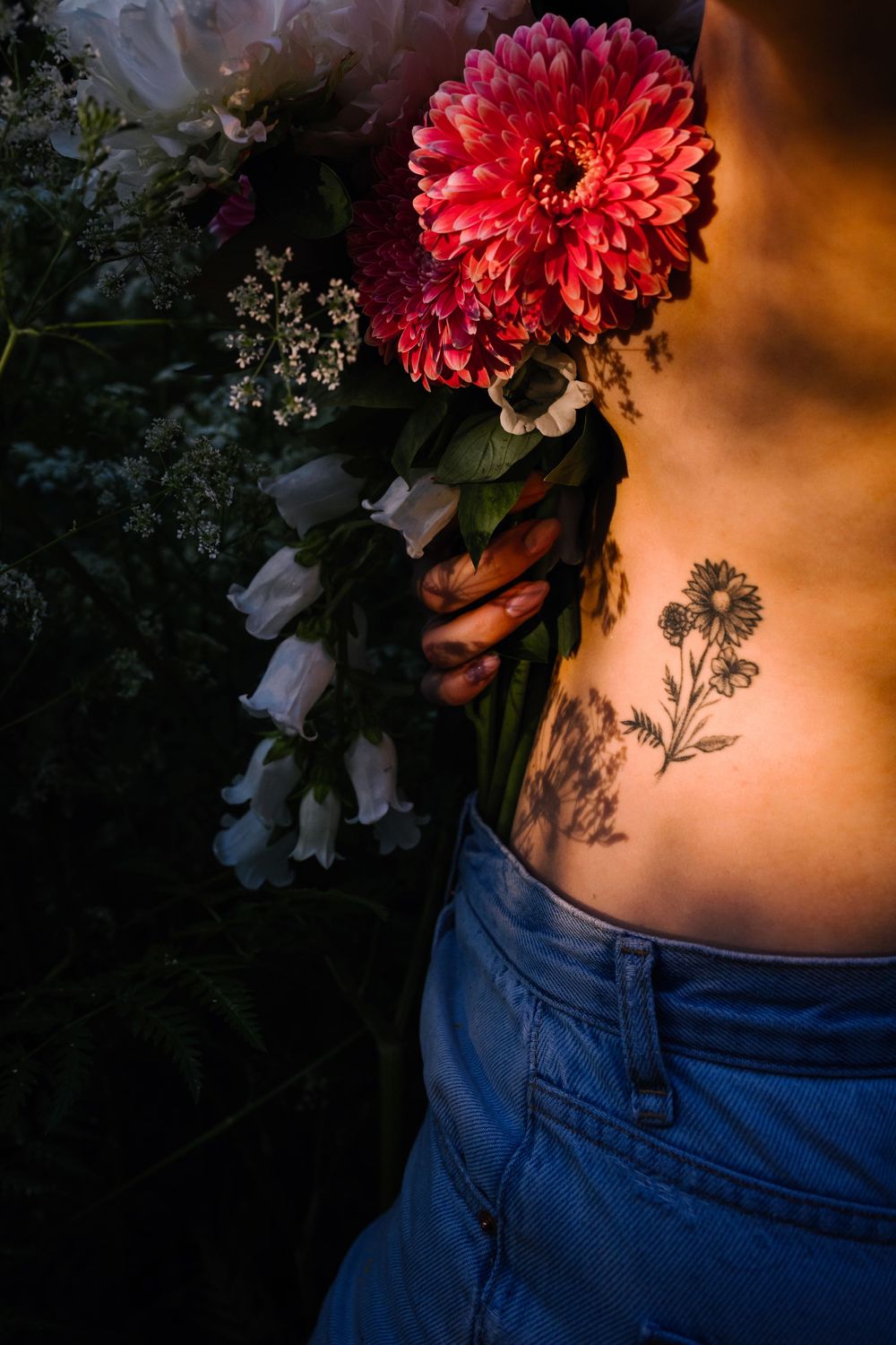 A vibrant red carnation flower against denim jeans and warm lighting creates a sensual artistic composition.