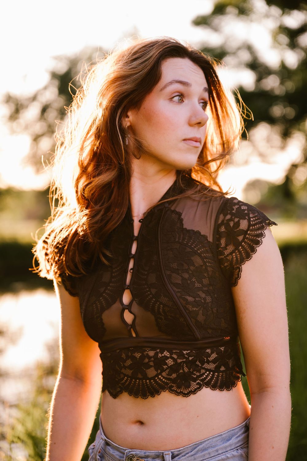 Sun-backlit portrait of someone in a black lace crop top and jeans outdoors during golden hour.