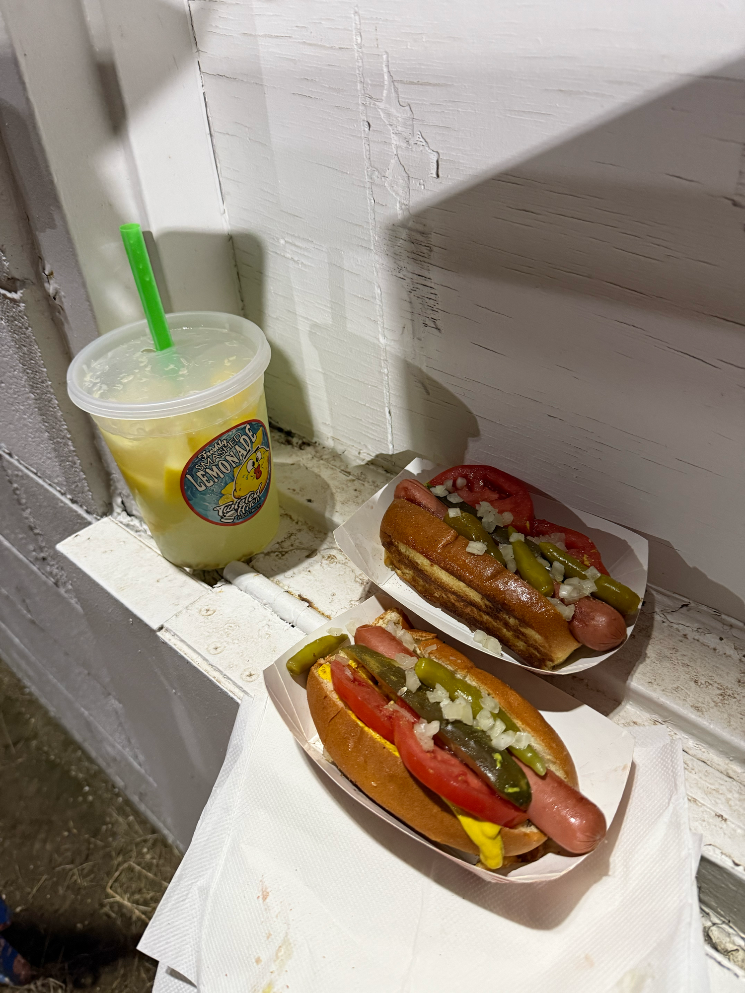 Hot dogs topped with various toppings and condiments served with a cold beverage on a white counter.