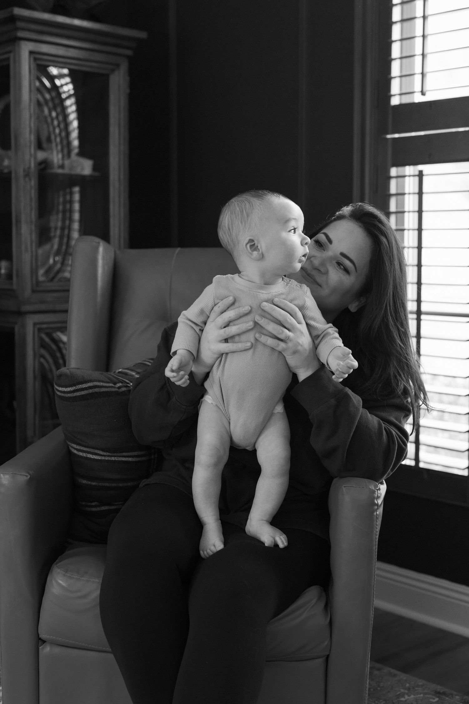 A sequence of black and white photos showing tender moments between a parent and baby interacting playfully at home.