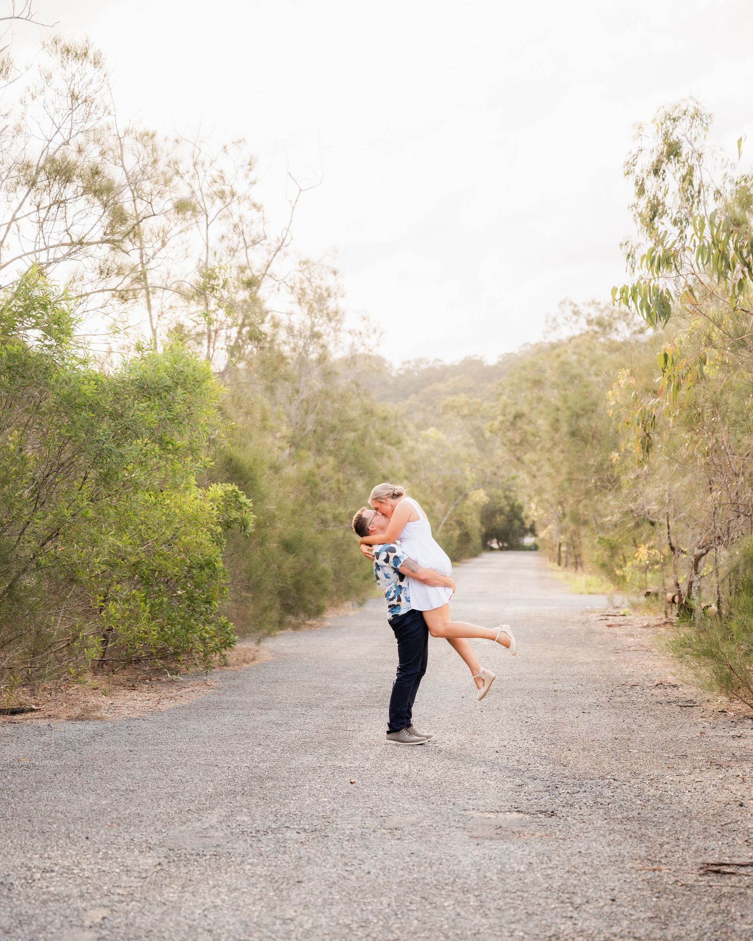 A couple dances together on a path surrounded by tall grass in a peaceful outdoor setting. Engagement session Gold Coast.