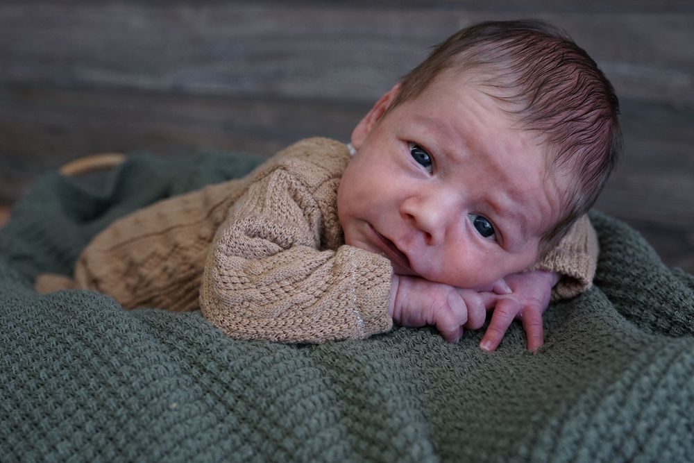 Adorable baby in a cozy knit sweater laying on a green textured blanket.