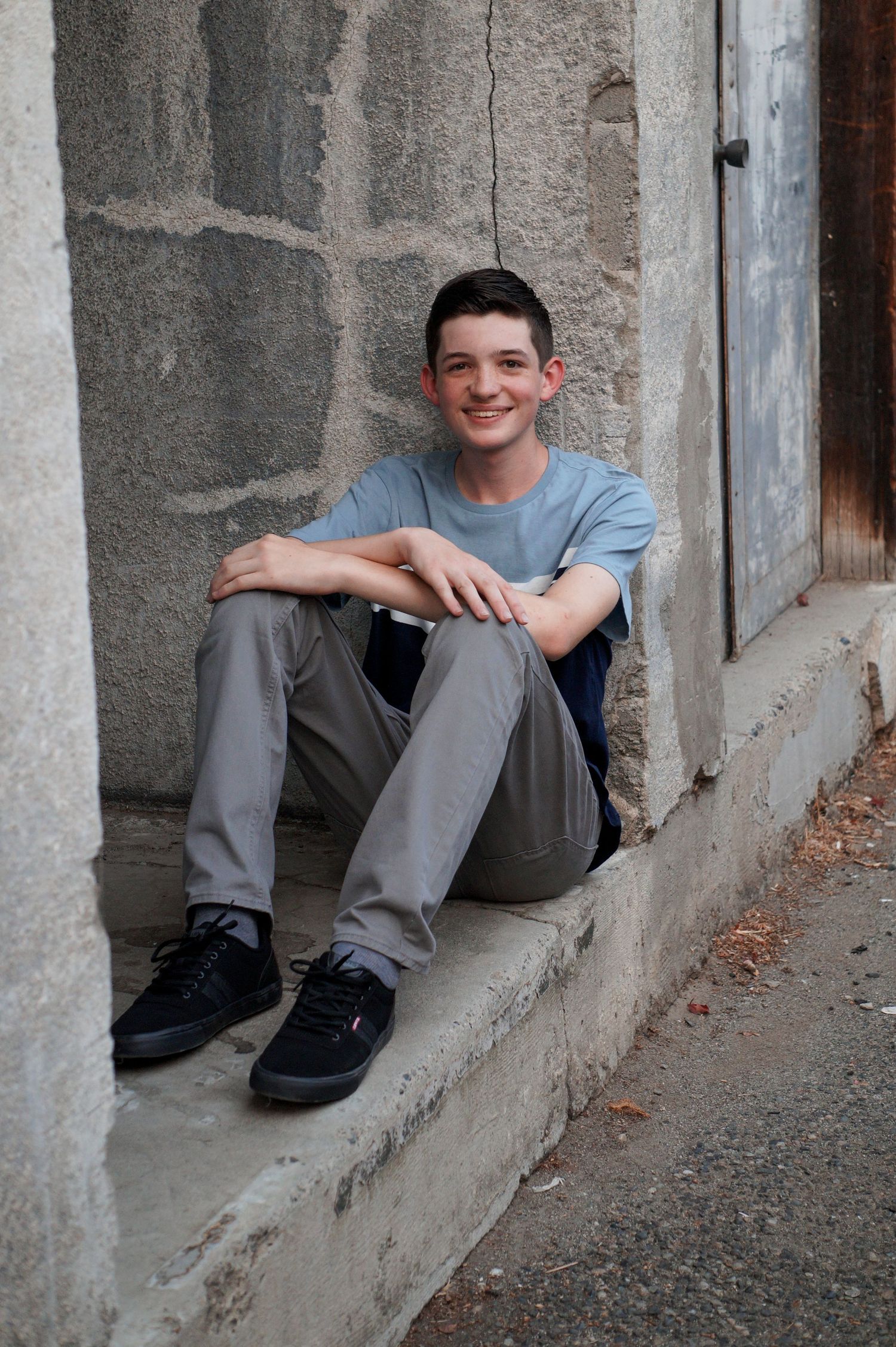 Casual senior portrait of teen boy sitting on sidewalk during urban senior session in Richland WA