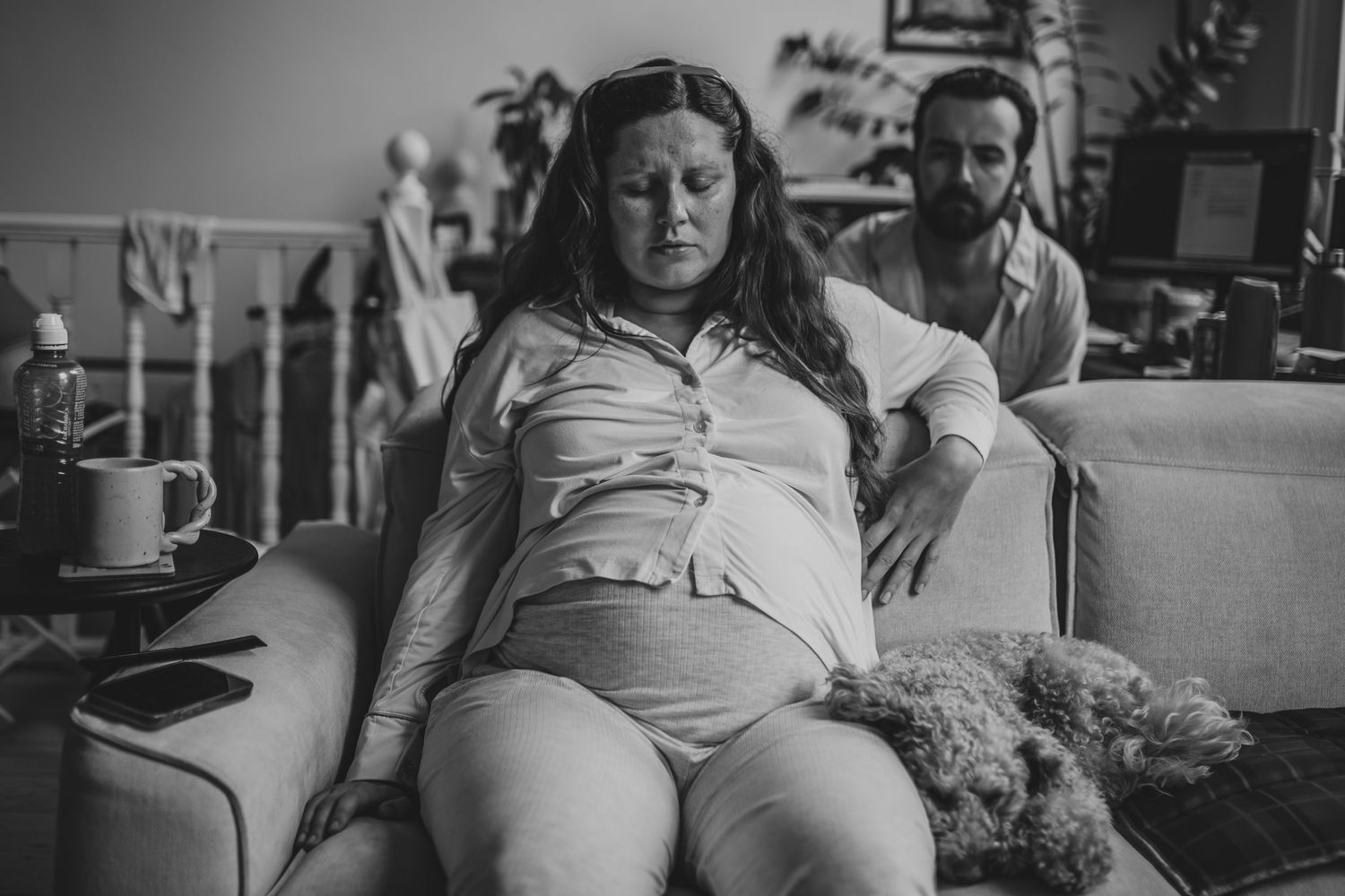 A monochrome photograph shows a person reclining with a relaxed posture on a couch during what appears to be a casual moment.