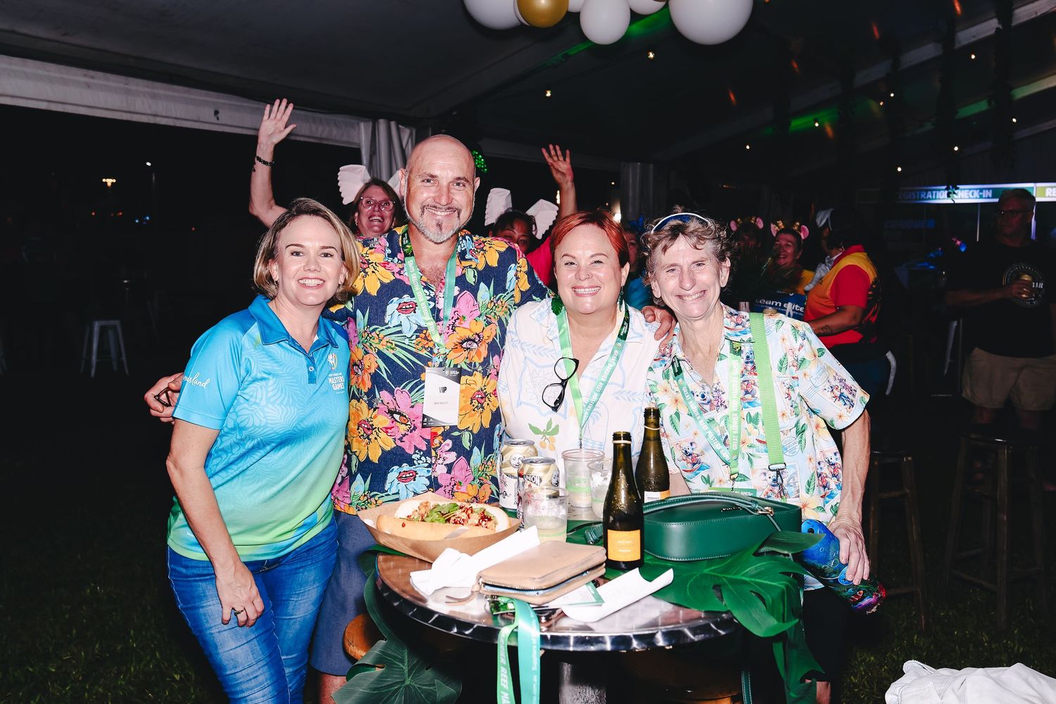 A group celebrating at a party with colorful balloons, drinks and snacks on the table in a dimly lit venue.