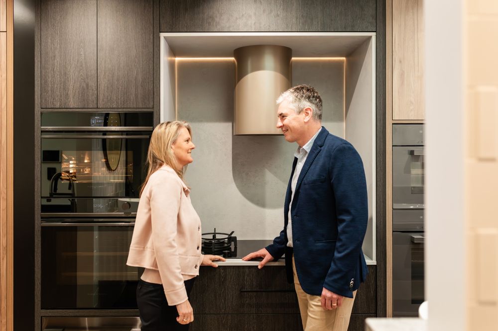 Contemporary kitchen showroom featuring dark wood cabinetry and stainless steel appliances.