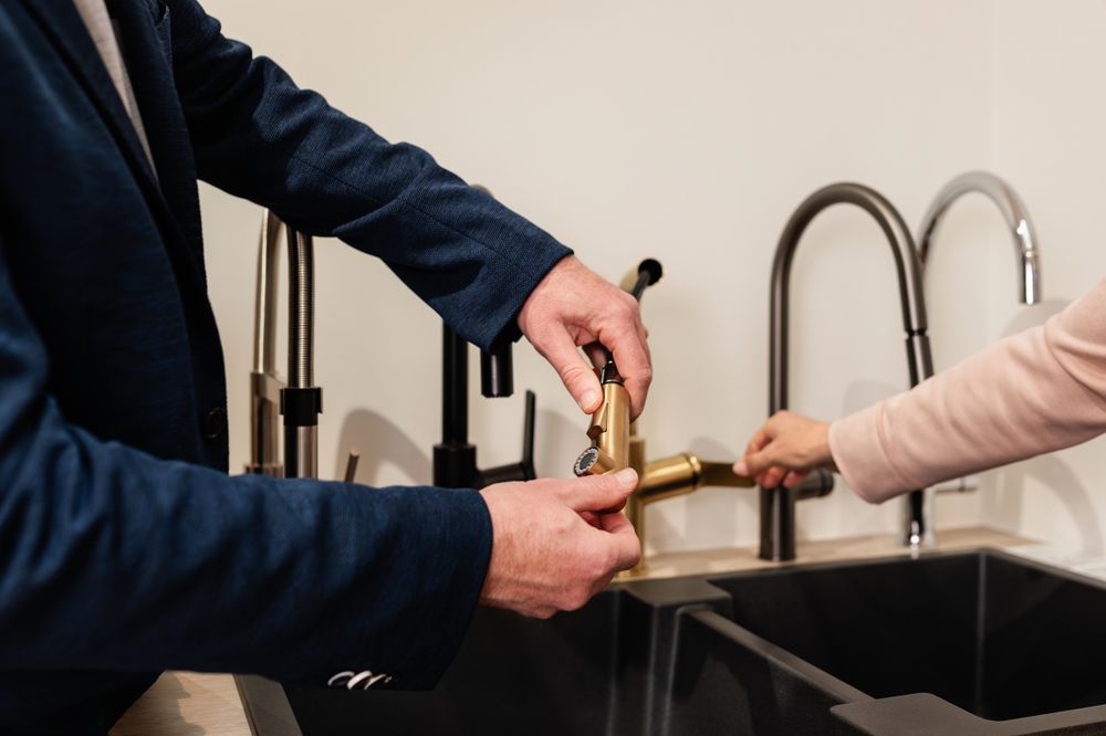 Hands pouring liquid from a glass bottle near a modern kitchen sink with matte black faucet.