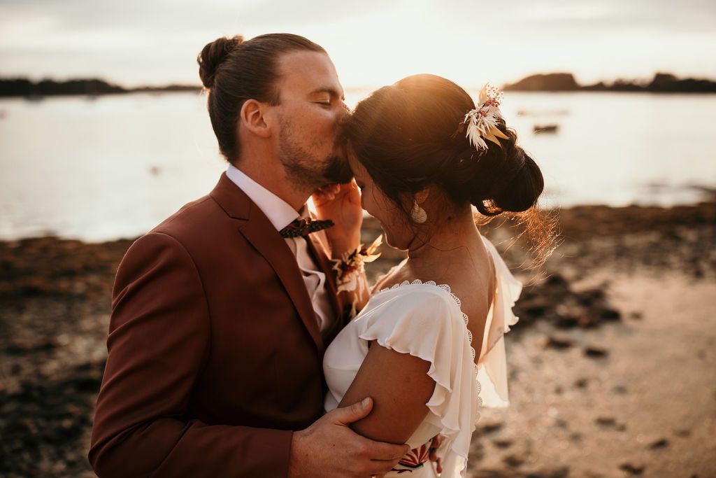 Intimate sunset wedding portrait on a rocky beach with warm golden light.
