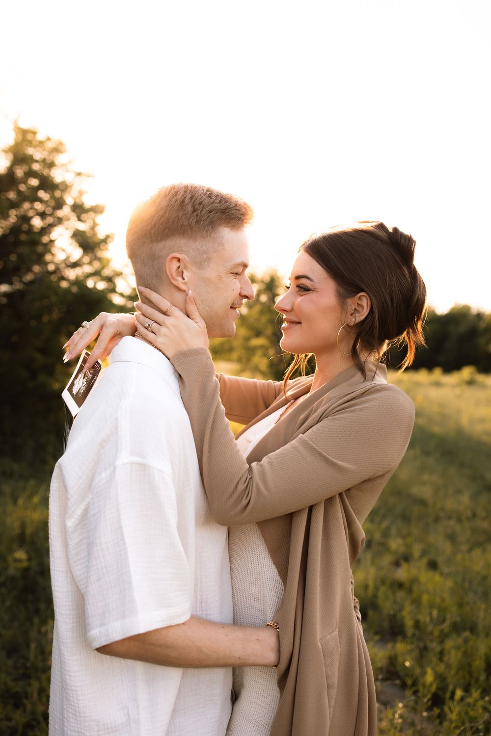 A romantic couple embraces in a sunlit meadow during a pregnancy announcement photoshoot.