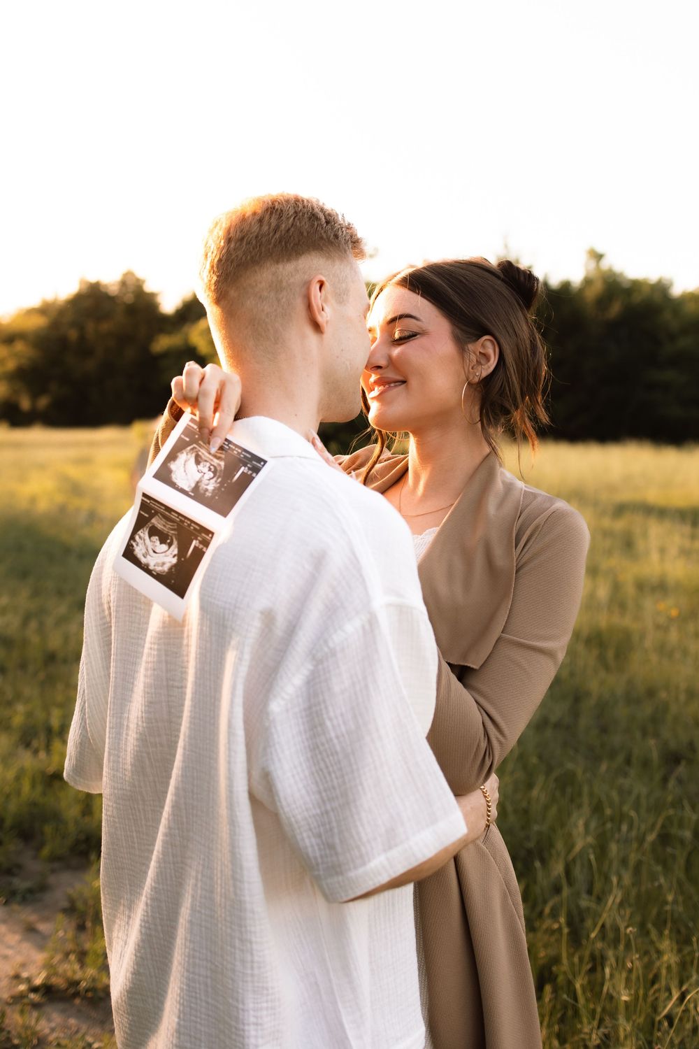 Intimate moment between couple sharing pregnancy news with ultrasound photos in a sunny field.