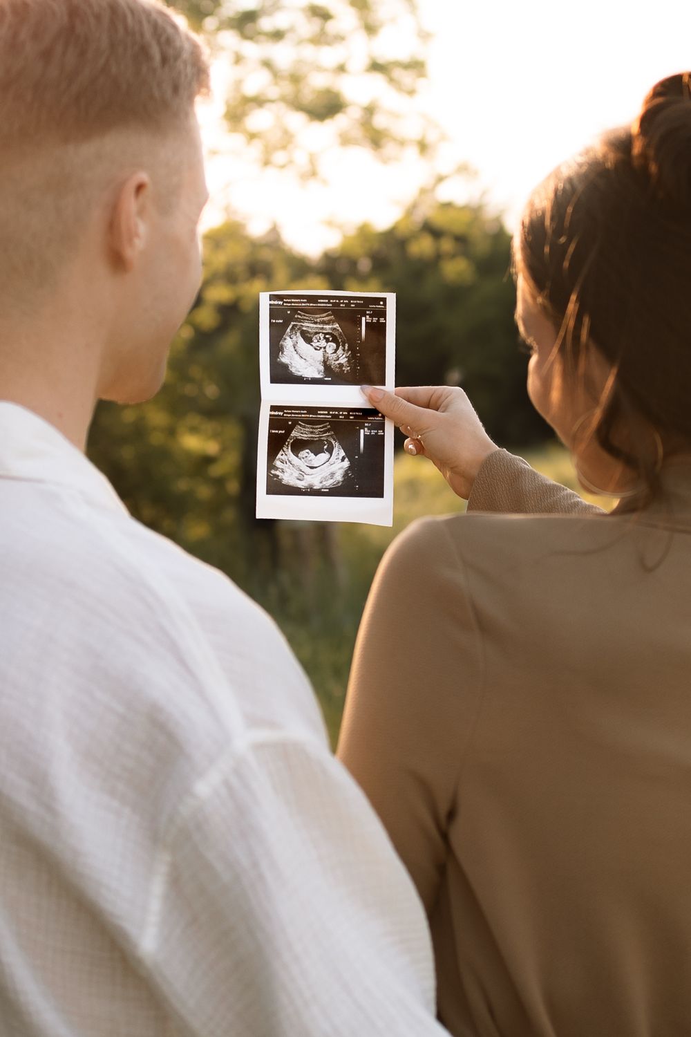 A couple looks at ultrasound photos together outdoors during golden hour sunset lighting.