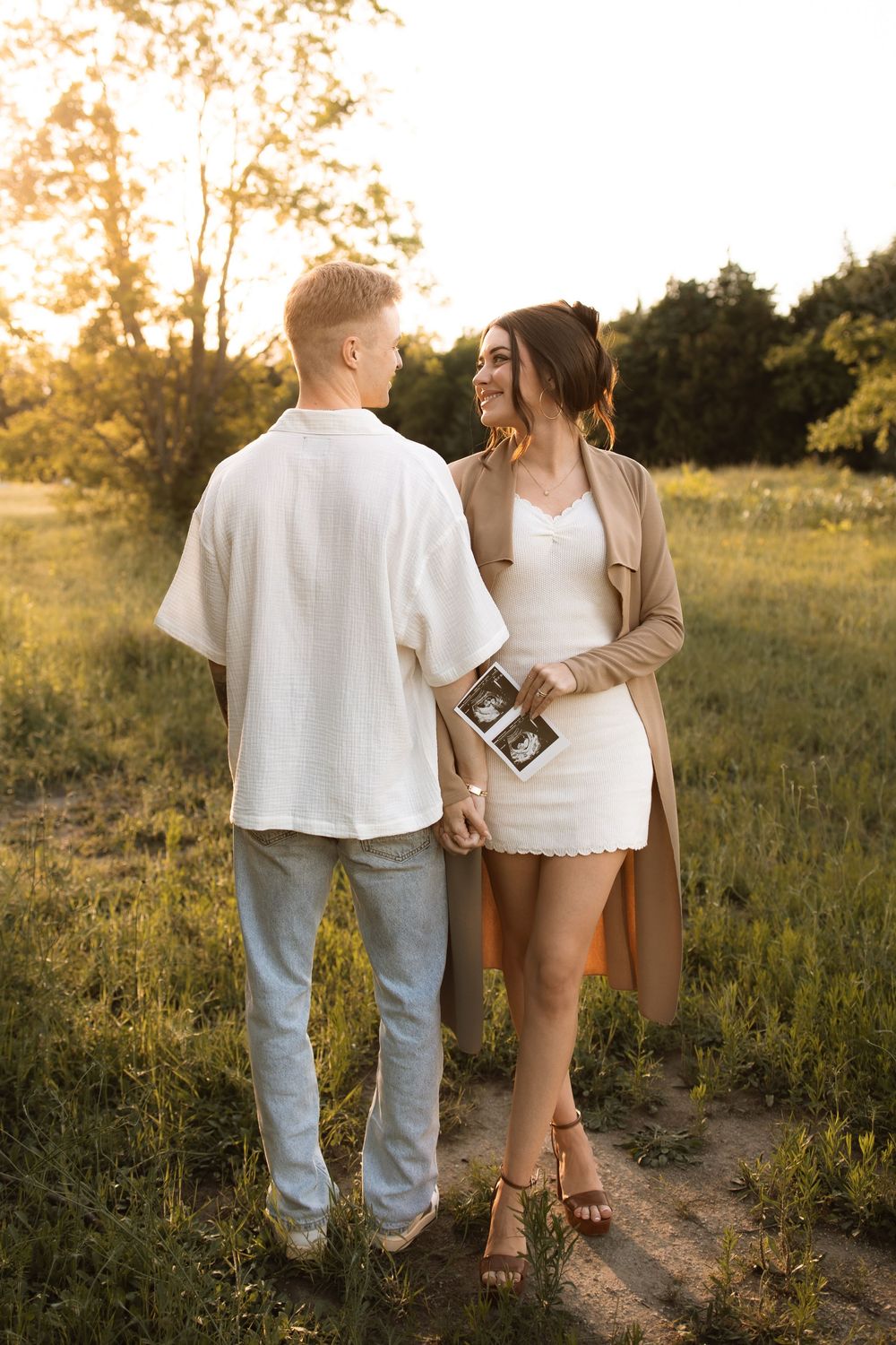 A couple wearing white and tan stand together on a dirt path during golden hour.