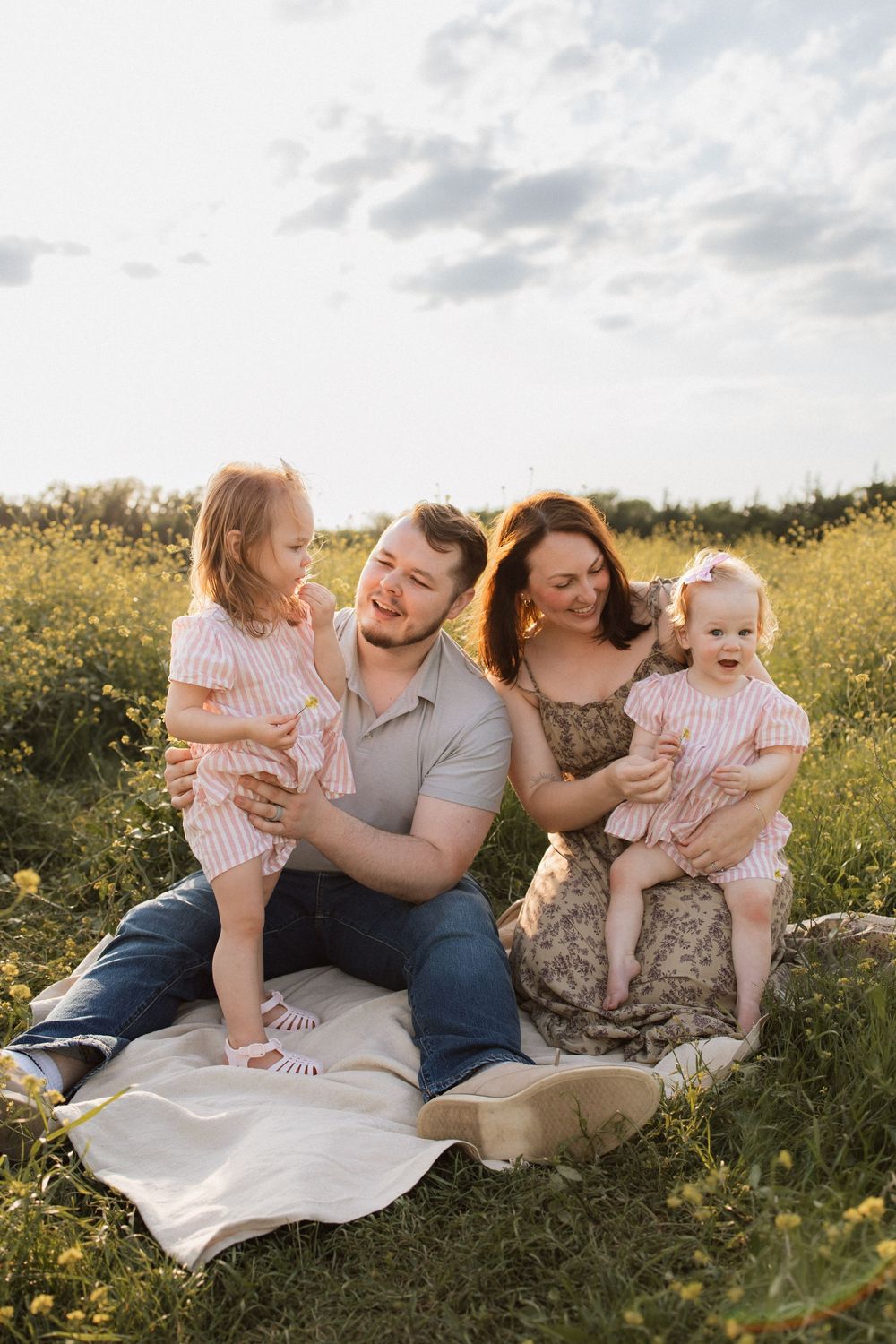 A family enjoys quality time together on a blanket in a sunny wildflower meadow during golden hour.