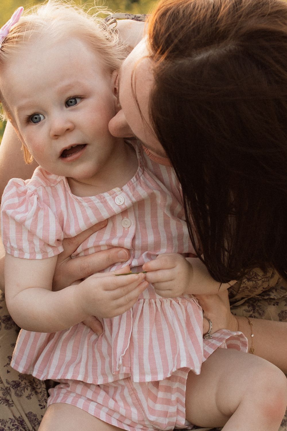 A baby wearing a pink and white striped dress is held in a series of intimate familial moments.