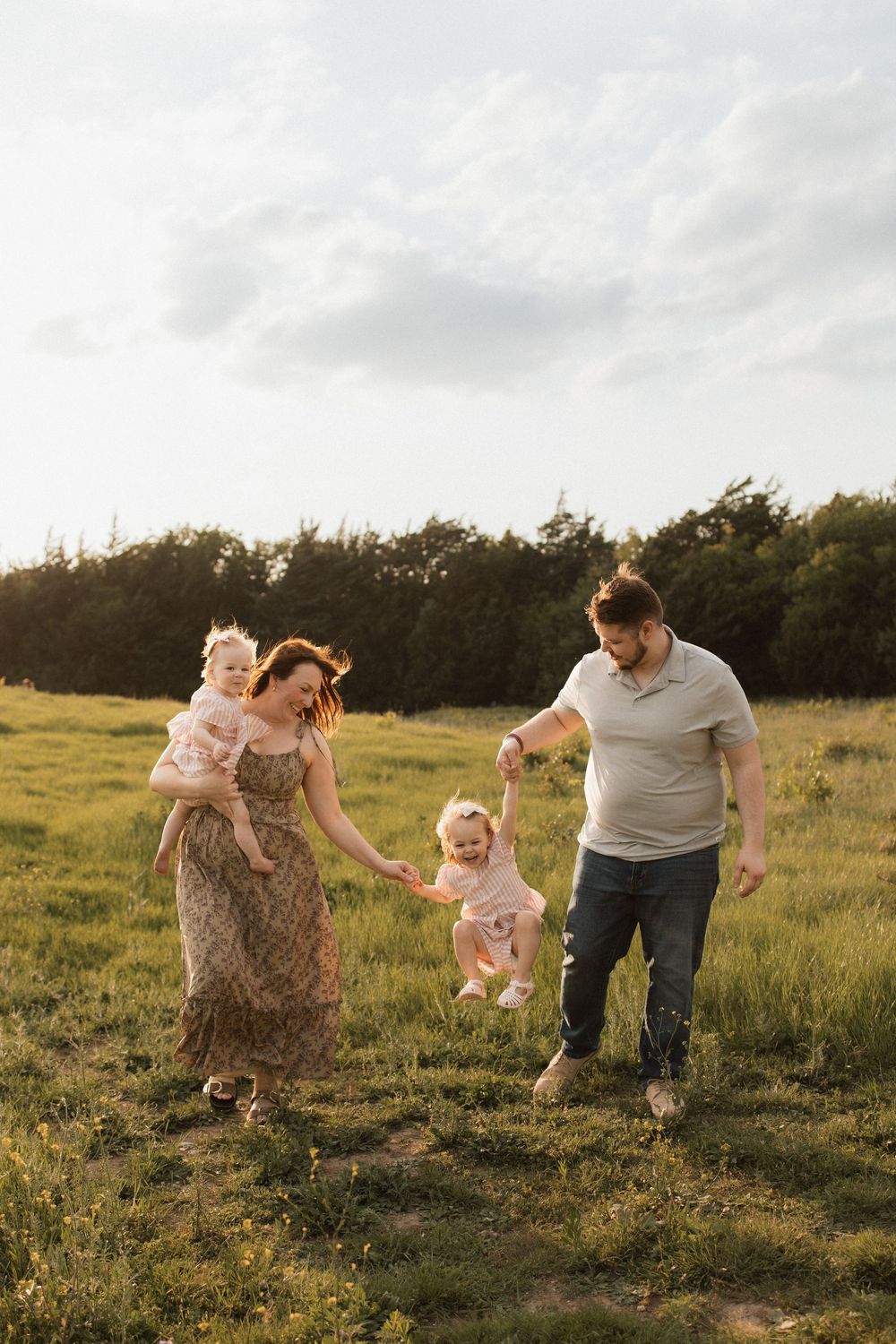 Family enjoying playful moment together in grassy field during golden sunset.