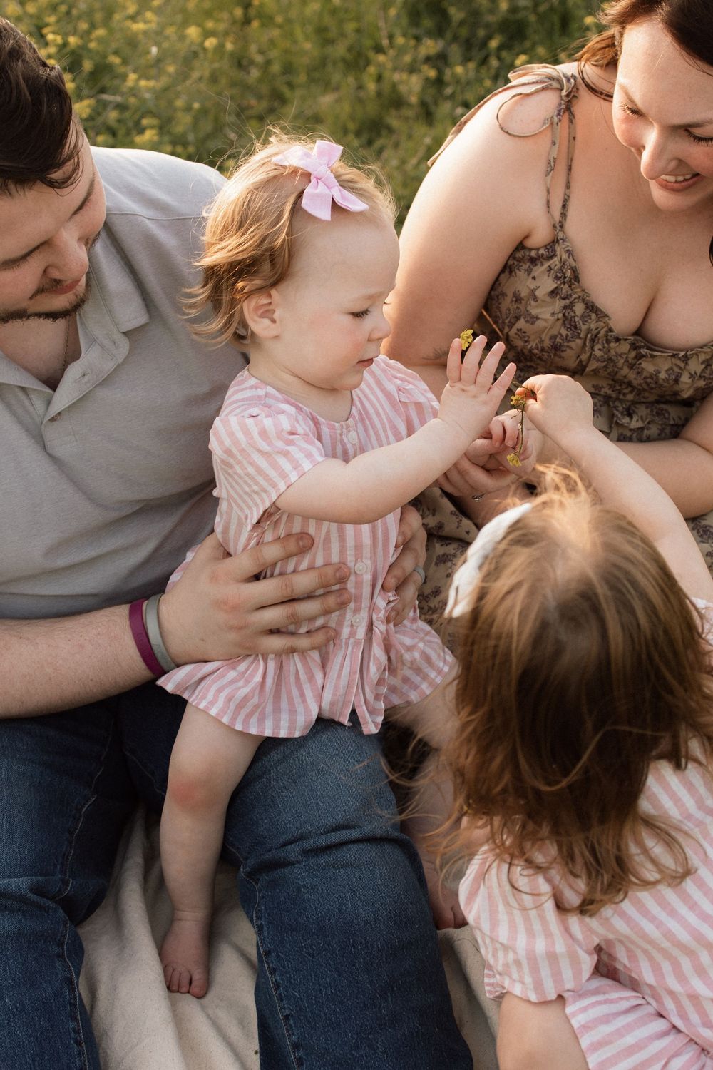 A tender family moment outdoors as they play together on a blanket, wearing pink and casual attire.