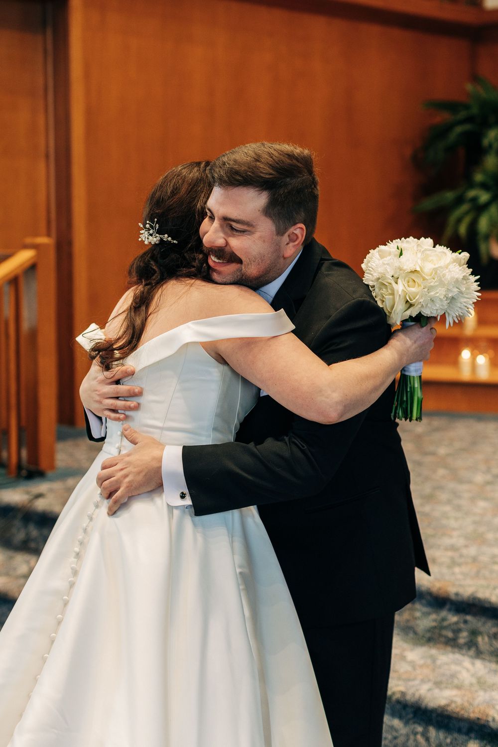 Emotional embrace between bride and groom during wedding ceremony with white bouquet.