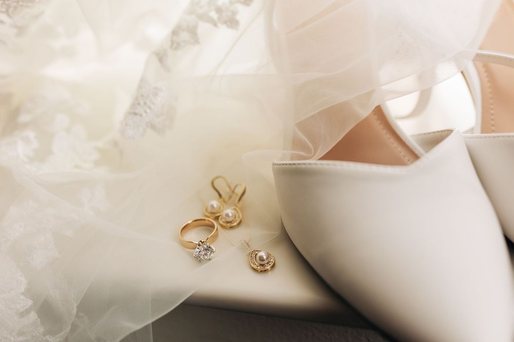 Golden wedding rings and earrings elegantly displayed next to a white bridal shoe and delicate tulle fabric.