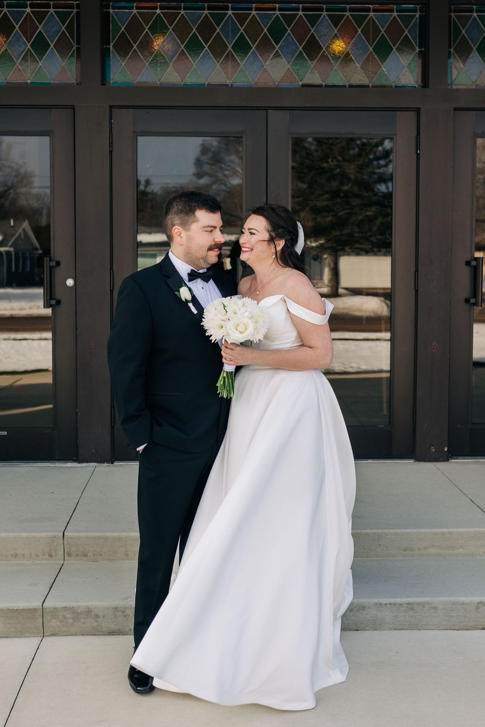 Newlyweds share a joyful embrace outside a modern building with geometric patterns.