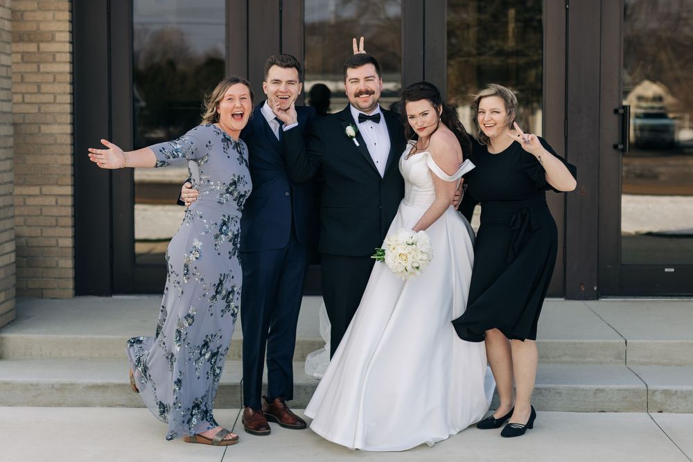 Wedding party gathered outside brick building posing for formal photos.