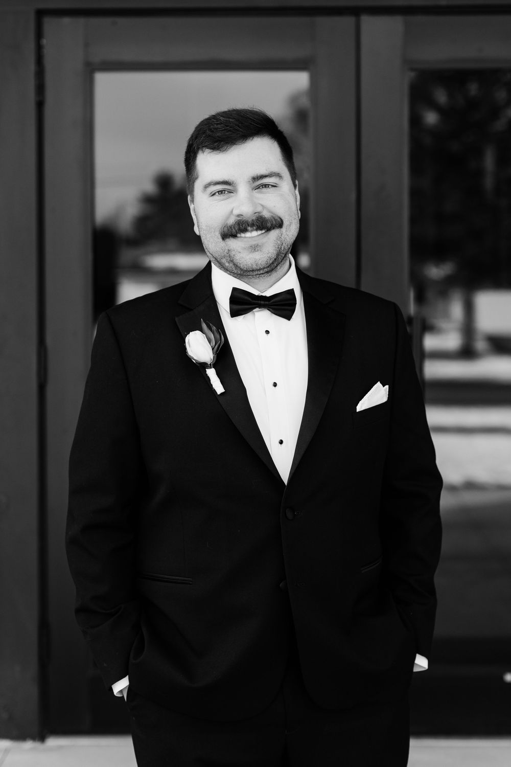 Formal portrait of groom in classic black tuxedo and bowtie against dark background.