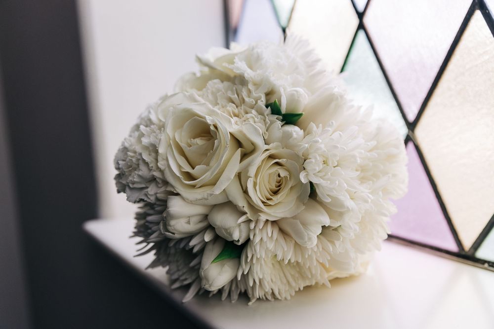 White carnations and roses arranged in a romantic bridal bouquet against a dark background.